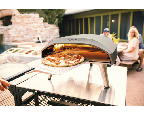Ooni Pizzaofen mit Pizza auf Pizzaschieber im Aussenbereich