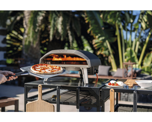 Ooni Pizzaofen mit Pizza auf Pizzaschieber auf einem Tisch im Freien
