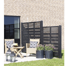 Terrasse mit Windschutzwand, Rattansesseln, Tisch, Laternen und Pflanzenkübeln vor einer Hauswand