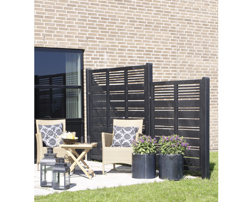 Terrasse avec pare-vent, fauteuils en rotin, table, lanternes et bacs à plantes devant un mur de maison