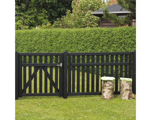 Schwarzer Gartenzaun mit Holztor und Baumstümpfen mit Kissen auf einer Rasenfläche