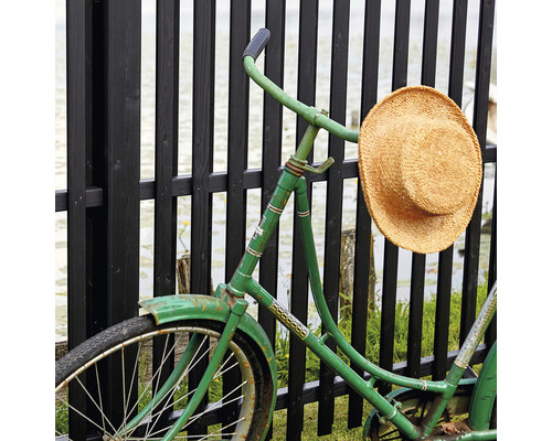 Ein grünes Fahrrad mit einem Strohhut lehnt an einem Zaun.