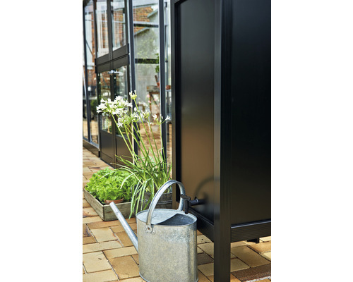 Regenwassertank mit Giesskanne und Pflanzen vor einem Gewächshaus