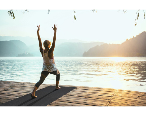 Frau macht Yoga auf einer Matte am See
