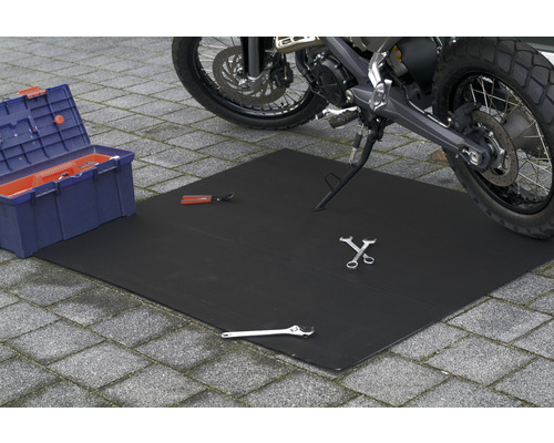 Eine schwarze Werkstattmatte liegt unter einem Motorrad, zusammen mit einem Werkzeugkasten und verschiedenen Werkzeugen.