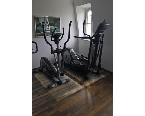 Deux vélos elliptiques dans une pièce avec plancher en bois et une fenêtre.