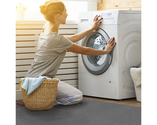 Frau bedient Waschmaschine auf einer grauen Fußmatte im Badezimmer