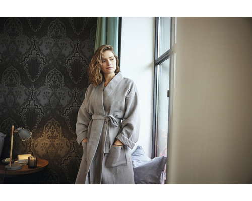 Femme en peignoir gaufré gris dans une pièce avec du papier peint à motifs
