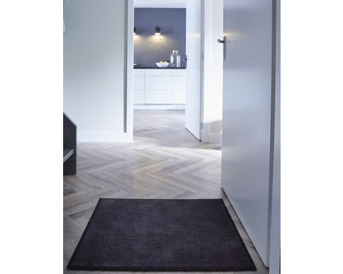 Couloir avec paillasson, plancher en bois et vue sur la cuisine