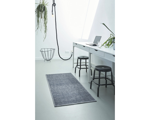 Ein heller Raum mit einem grauen Teppich, einem weißen Schreibtisch und zwei Hockern