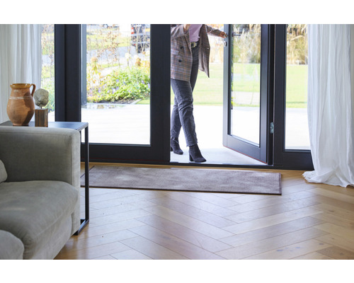 Zone d''entrée avec paillasson, plancher en bois et une femme qui passe une porte