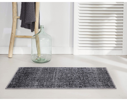 Tapis de bain gris devant un mur avec échelle en bois et bouteille décorative