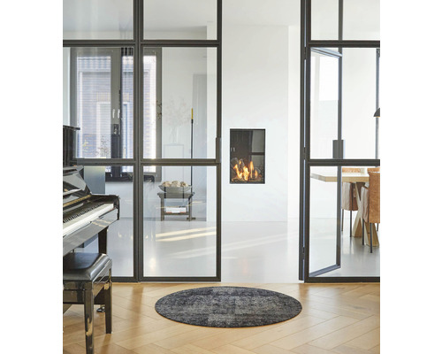 Salon avec portes coulissantes en verre, cheminée, piano et tapis rond sur parquet.