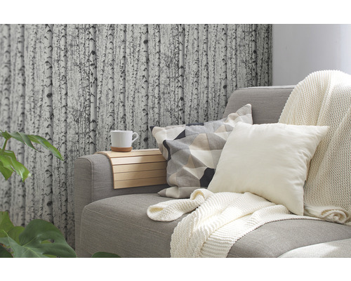 Salon avec canapé gris, coussins, couverture et papier peint à motif de bouleau