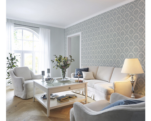Salon avec canapé, fauteuils, table basse, lampadaire et papier peint à motifs pour un aménagement élégant.