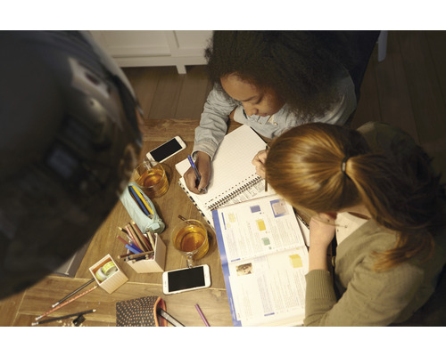 Zwei Personen lernen gemeinsam an einem Holztisch mit Notizblöcken, Stiften, Mobiltelefonen und Getränken.