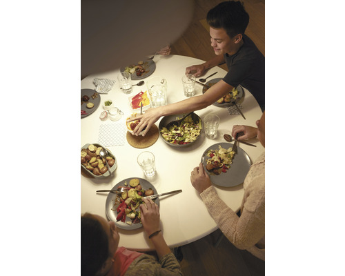 Familie sitzt an einem runden Tisch beim Essen mit Salaten und Kartoffeln.