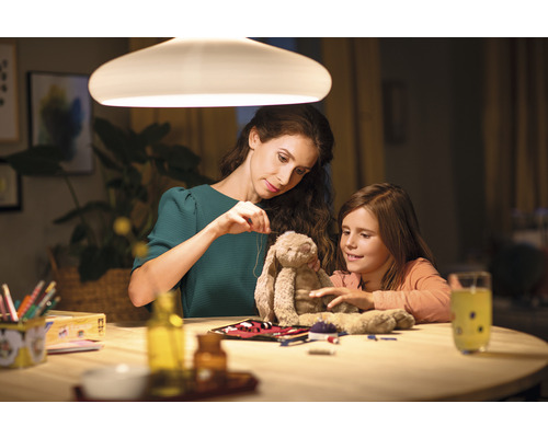 Une mère et sa fille sont assises à une table sous une lampe et réparent une peluche.