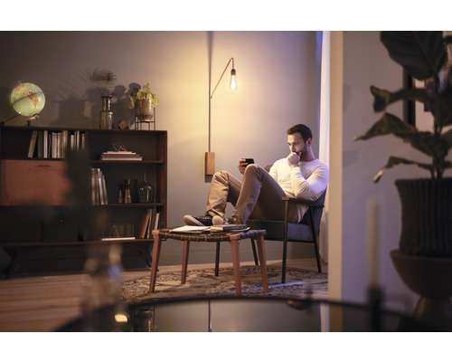 Wohnzimmer mit Mann im Sessel, Stehleuchte und Bücherregal für eine gemütliche Atmosphäre