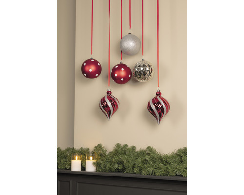 Boules de Noël décoratives avec des rubans rouges devant un mur et une guirlande verte.