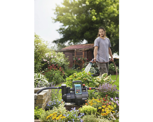 Garten mit Hauswasserwerk und Person, die mit einem Schlauch gießt