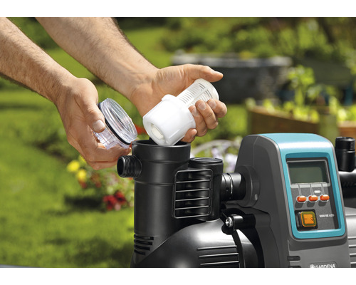 Mann setzt Filter in eine Hauswasseranlage im Garten ein.
