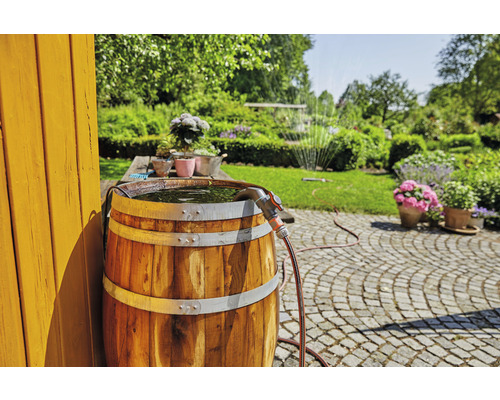 Récupérateur d''eau de pluie en bois rempli d''eau et d''un tuyau d''arrosage dans un jardin ensoleillé.