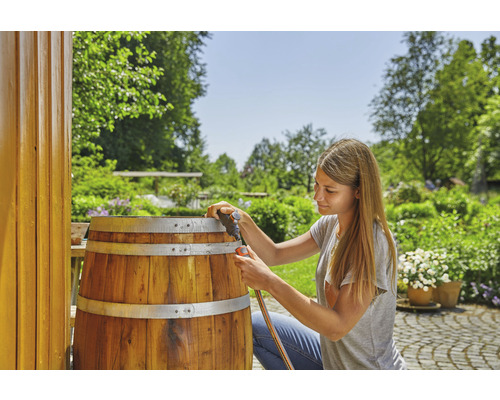 Une femme raccorde un tuyau d''arrosage à une cuve à eau de pluie en bois dans le jardin.