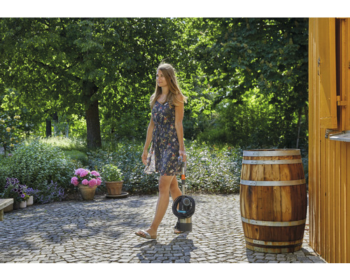 Une femme se promène dans un jardin avec une pompe à baril Gardena.