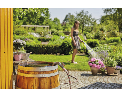 Récupérateur d''eau de pluie en bois dans le jardin, une femme arrose les plantes