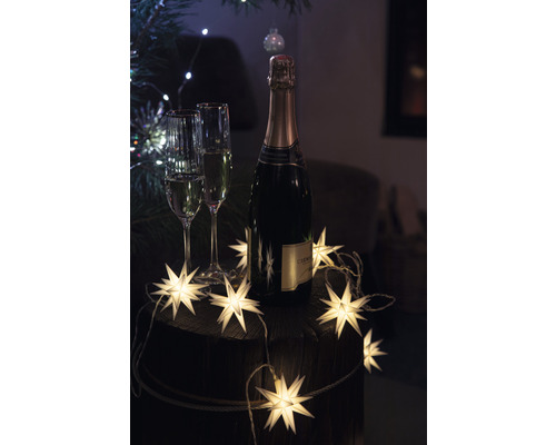 Champagnerflasche und zwei Gläser mit Sternenlichterkette auf einem Fass