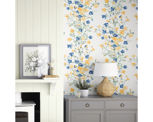 Intérieur décoratif avec papier peint à motifs floraux, commode, lampe et cheminée.