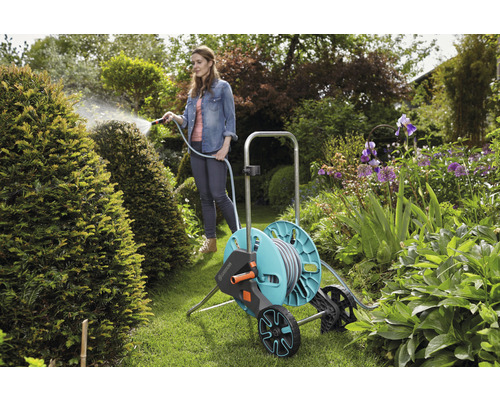 Frau bewässert Pflanzen mit einem Gartenschlauch auf einer Schlauchwagen im Garten.