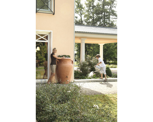 Femme près d''une cuve de récupération d''eau de pluie en forme d''amphore et enfant arrosant des plantes dans le jardin