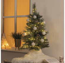 Sapin de Noël artificiel décoré avec éclairage, boules et pommes de pin dans un espace de vie