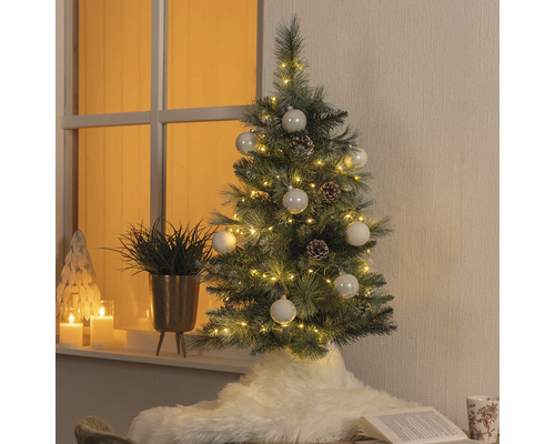 Sapin de Noël artificiel décoré avec éclairage, boules et pommes de pin dans un espace de vie
