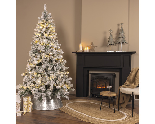 Festlich geschmückter Weihnachtsbaum mit Beleuchtung, Baumschmuck und Weihnachtsgeschenken neben einem Kamin