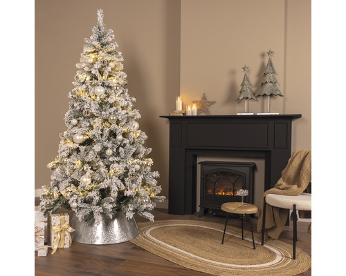 Festlich geschmückter Raum mit schneebedecktem Weihnachtsbaum, Kamin und Dekorationen.