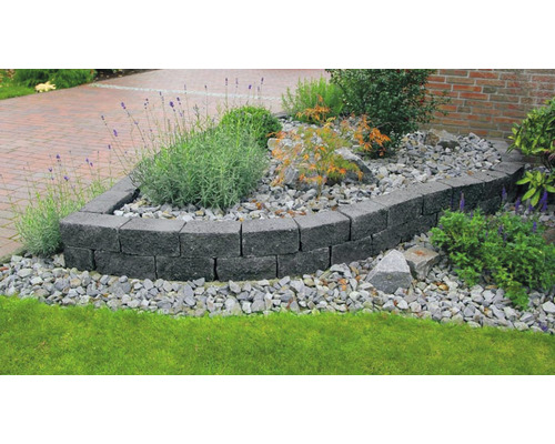 Aménagement de jardin avec un mur en blocs de béton gris, entouré de plantes et de pierres.