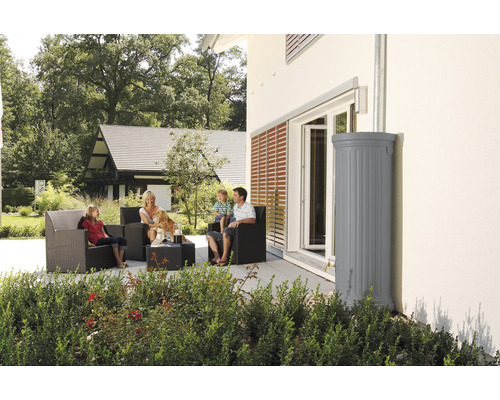 Une famille est assise sur la terrasse à côté d''une cuve de récupération d''eau de pluie grise près de la maison.