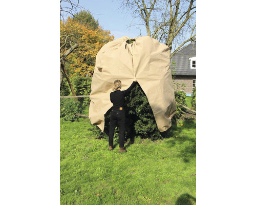 Une femme recouvre un arbuste dans le jardin avec une housse pour plantes.