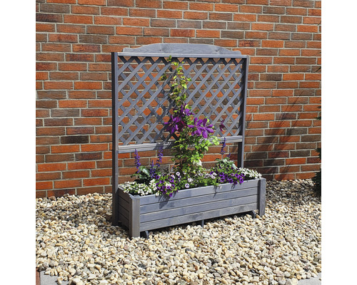 Holz Pflanzkasten mit Rankgitter und blühenden Pflanzen vor einer Backsteinmauer.