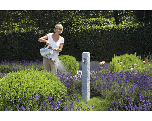Frau gießt Pflanzen in einem Garten mit einem Wasserhahn aus Stein und Lavendel