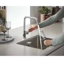 Une personne remplit un verre d''eau à partir d''un robinet de cuisine chromé.