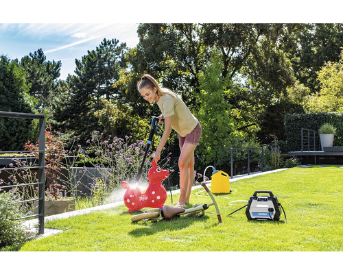 Frau reinigt mit einem Hochdruckreiniger im Garten ein Kinderspielzeug.