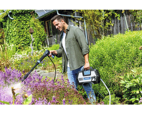 Un homme utilise un nettoyeur haute pression Gloria dans le jardin pour arroser les plantes.