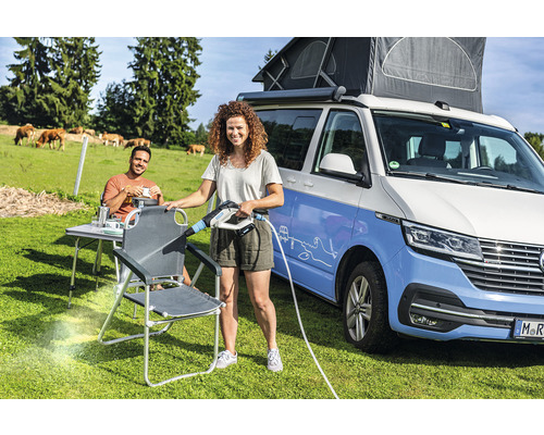 Frau reinigt Campingstuhl mit Akku-Reiniger neben Campingbus