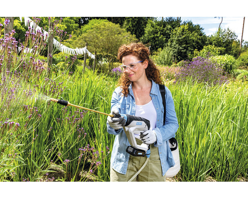 Frau mit Akku-Sprühgerät im Garten bei der Pflanzenpflege.