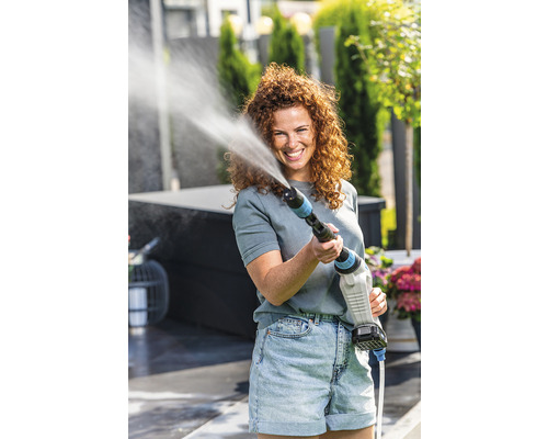Frau benutzt einen Akku-Hochdruckreiniger im Garten.