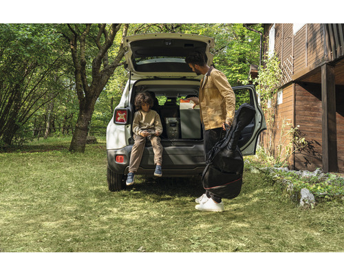 Szene im Freien mit einem Mann, der eine Tragetasche hält, und einem Kind, das im Kofferraum eines Autos sitzt, neben einer tragbaren Powerstation